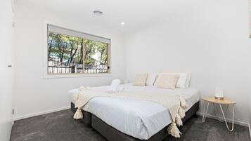A bedroom with a large bed, a window with a view, and a bedside table with a lamp.