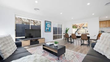 A modern living room with a flat-screen TV, a coffee table, and a dining area with chairs and a table.