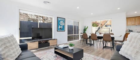 A modern living room with a flat-screen TV, a coffee table, and a dining area with chairs and a table.