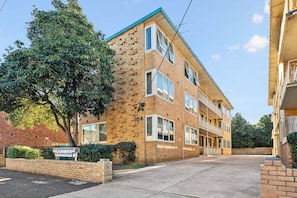 A multi-story brick building with a flat roof, large windows, and a visible balcony on the second floor. - Domi Rentals - The Carlisle Street Apartments (Balaclava)
