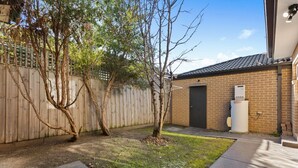 A backyard with a wooden fence, a brick building, and a small tree. - Domi Rentals The Blackburn Residence (Notting Hill)
