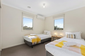 A hotel room with two beds, a small bedside table, an air conditioning unit, and a window with a view.
