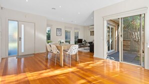 A spacious room with a wooden floor, a dining area with chairs, a TV, and a sliding glass door leading to an outdoor area. - Domi Rentals The Blackburn Residence (Notting Hill)