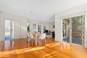 A spacious room with a wooden floor, a dining area with chairs, a TV, and a sliding glass door leading to an outdoor area.