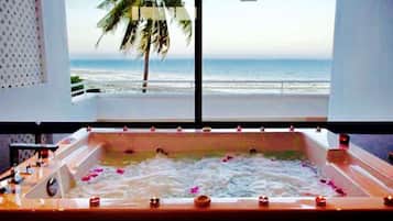 A bathtub with rose petals and candles, overlooking a beach with palm trees and the ocean.