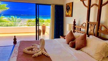 A hotel room with a bed, a view of the ocean, a large vase, and a welcome mat.