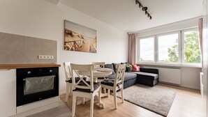 A modern kitchen with an oven, dining table, and chairs, a gray sofa, and a large window with a view. - Przymorze Seaside Comfort Studio (Gdańsk)
