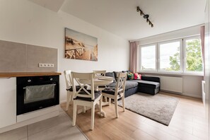 A modern kitchen with an oven, dining table, and chairs, a gray sofa, and a large window with a view. - Przymorze Seaside Comfort Studio (Gdańsk)