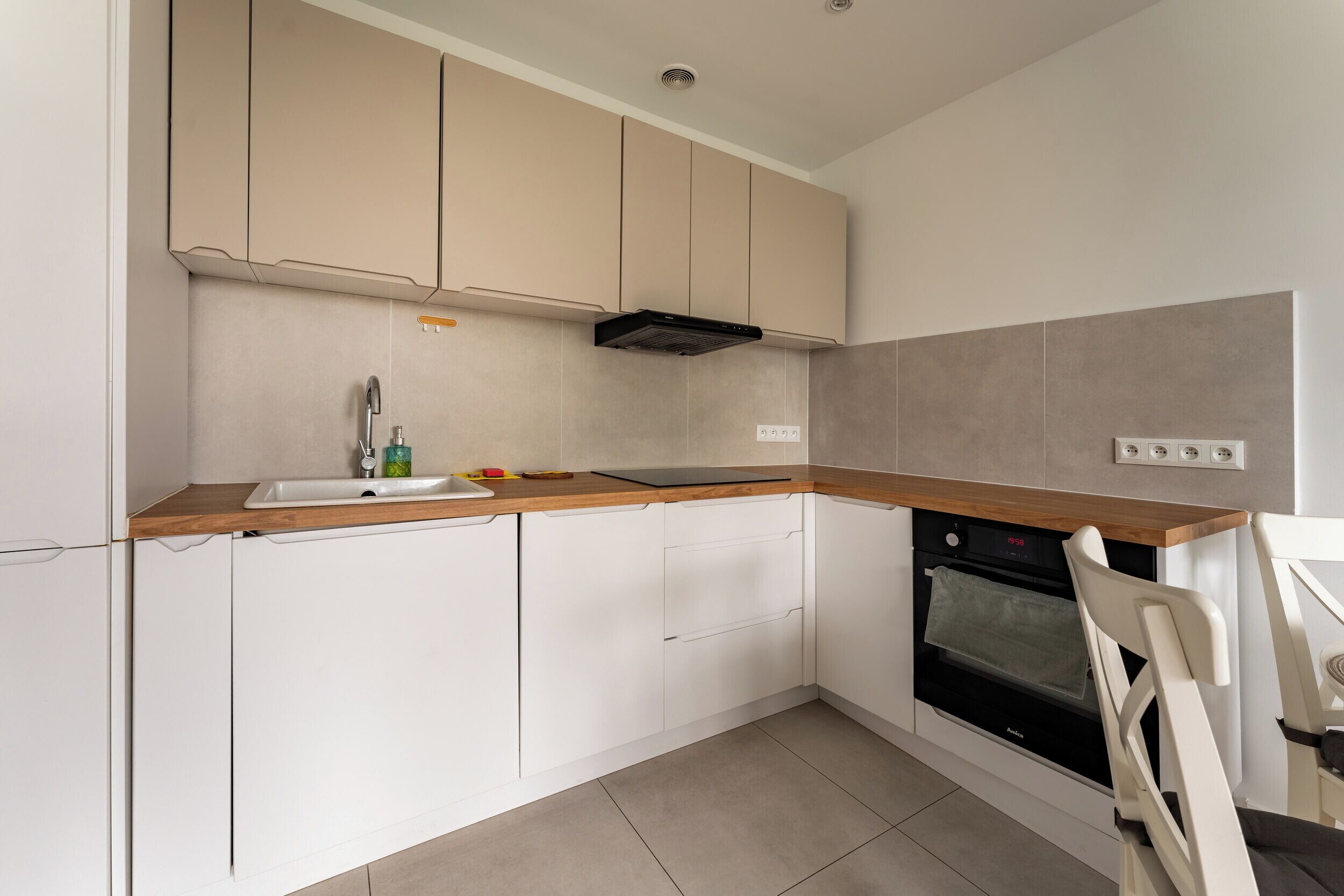 A modern kitchen with white cabinets, a wooden countertop, a built-in oven, and a chair.