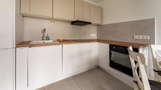 A modern kitchen with white cabinets, a wooden countertop, a built-in oven, and a chair. - Przymorze Seaside Comfort Studio (Gdańsk)