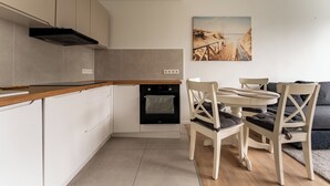 A modern kitchen with a built-in oven and a dining area with a round table and chairs. - Przymorze Seaside Comfort Studio (Gdańsk)