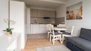 A modern kitchen with white cabinets, a dining table with chairs, and a grey sofa. - Przymorze Seaside Comfort Studio (Gdańsk)