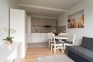 A modern kitchen with white cabinets, a dining table with chairs, and a grey sofa. - Przymorze Seaside Comfort Studio (Gdańsk)