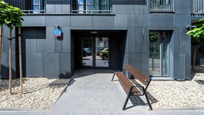 Een modern gebouw met een verharde entree, een bankje en een bord met het adres.