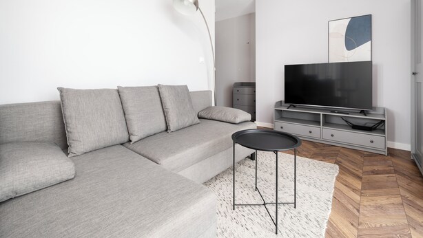 Een moderne woonkamer met een grijze bank, een zwarte salontafel, een flatscreen televisie en een minimalistische inrichting.