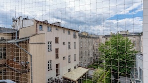 Un edificio residencial con múltiples ventanas, un balcón y un jardín visible a través de una malla metálica.