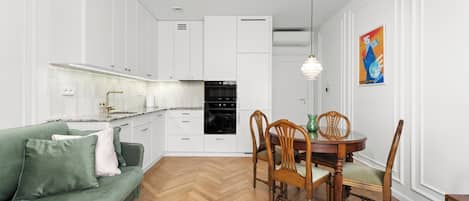 A modern kitchen with white cabinetry, a dining table with chairs, and a green sofa.