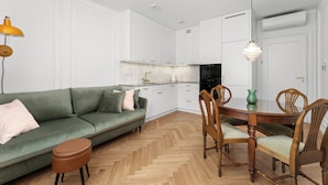 Una cocina moderna con armarios blancos, una mesa de comedor con sillas, un sofá verde y piso de madera.