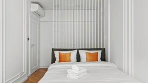 Habitación de hotel con cama, paredes blancas, ventana y equipo de aire acondicionado.