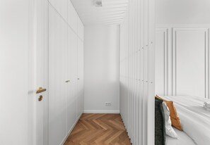A hallway with white walls, a wooden floor, and a bed with white bedding and an orange pillow. - Kamienica Pod Czaplą Heritage Apartment (Kraków)