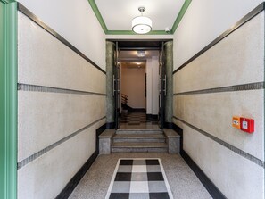 A hallway with a checkered floor, a staircase, and a fire alarm on the wall. - Kamienica Pod Czaplą Heritage Apartment (Kraków)