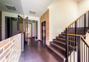 A modern hotel lobby with a brick accent wall, a staircase with wooden handrails, and a clean, tiled floor. - Cracow Novum Apartment #104 (Kraków)