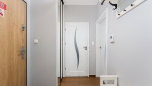 En hall med en dörr av trä, en vit dörr med en svängd design och en vit bänk.