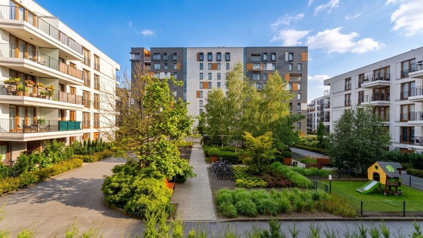 Ett bostadskomplex med flera balkonger, en central gångväg och en lekplats.