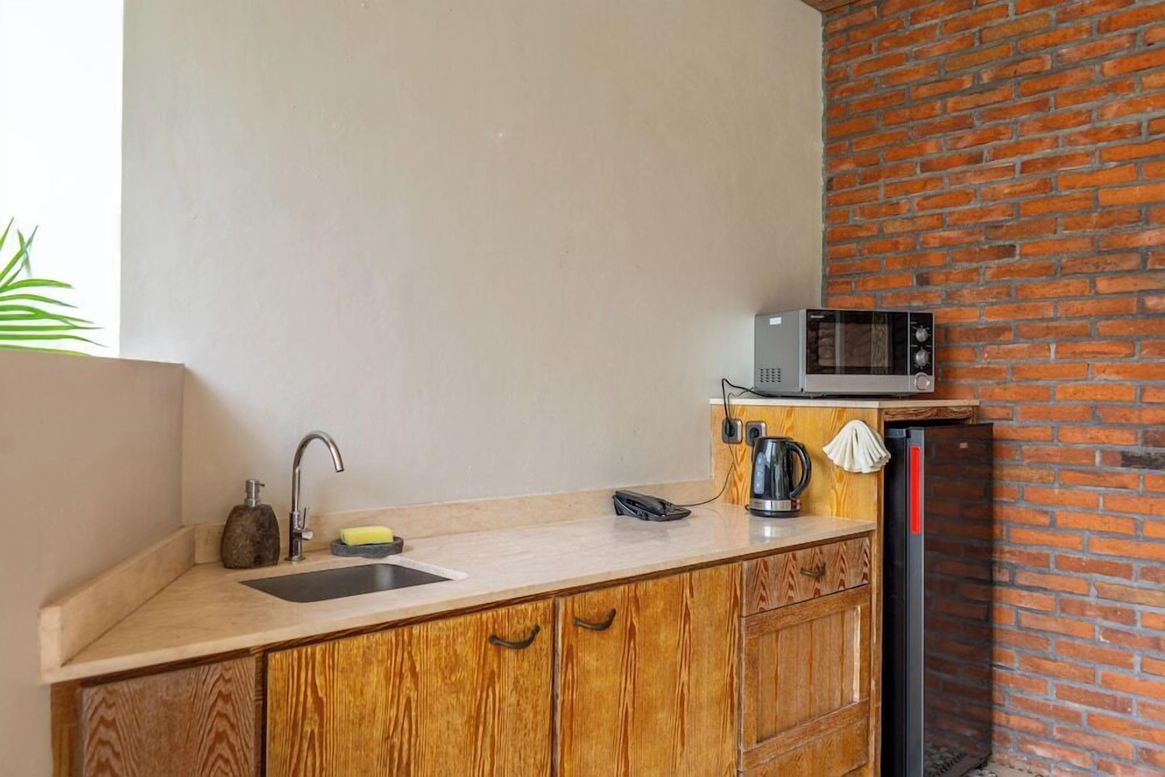 A kitchen with a wooden countertop, a sink, a microwave, and a brick wall.