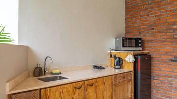 A kitchen with a wooden countertop, a sink, a microwave, and a brick wall.
