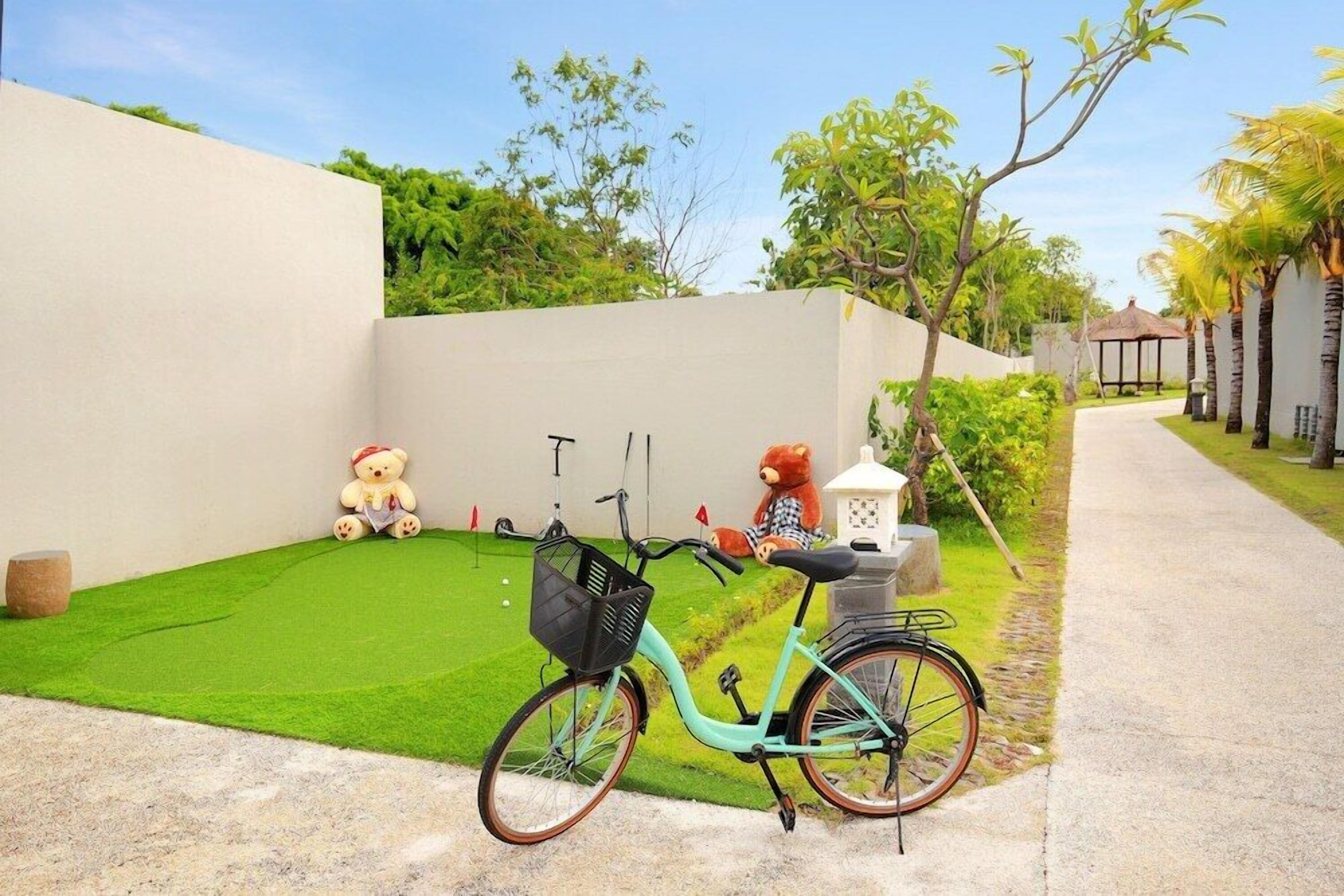 A bicycle parked on a green lawn with a white wall and a pathway leading to a gazebo.