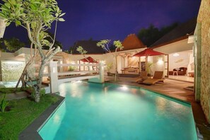 A swimming pool with lounge chairs and umbrellas, surrounded by a landscaped garden and a building with a tiled roof. - Vivara Private Pool Villas & Spa Retreat (Jimbaran)