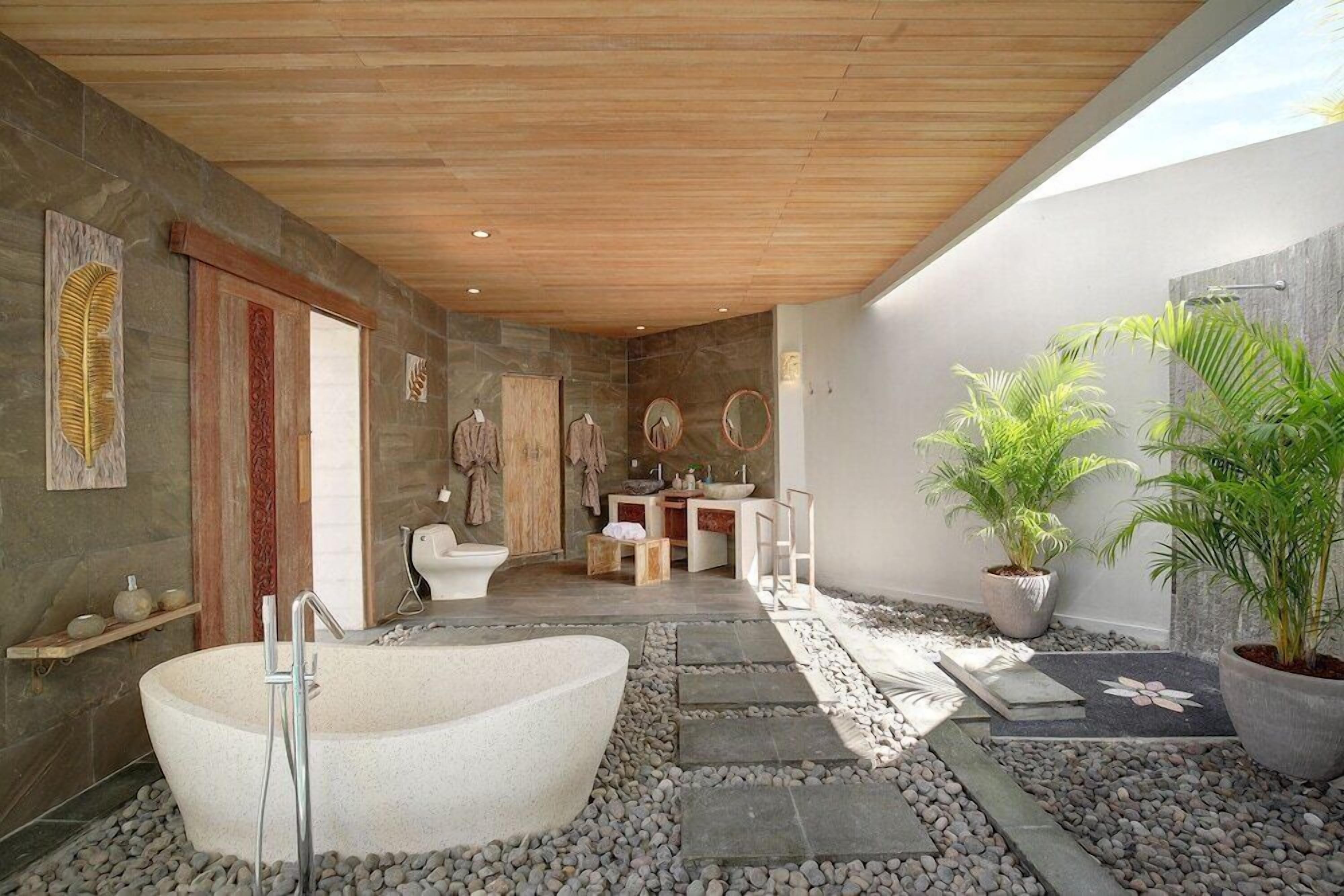A modern bathroom with a freestanding bathtub, stone walls, and a wooden ceiling.