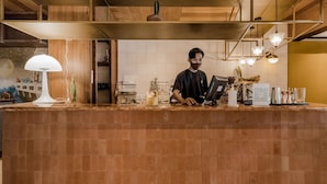 A barista at a counter with a coffee machine, a menu, and a decorative wall. - The House Tour Hotel Downtown (Bandung)