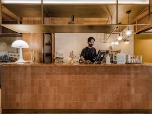 A barista at a counter with a coffee machine, a menu, and a decorative wall.