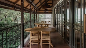 A covered outdoor area with wooden tables and chairs, a railing, and large windows. - The House Tour Hotel Downtown (Bandung)