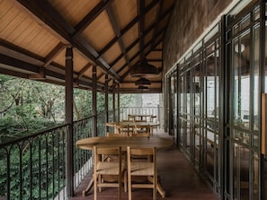 A covered outdoor area with wooden tables and chairs, a railing, and large windows.