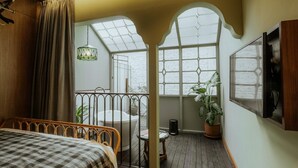 A bedroom with a large bed, a window with a view, a hanging light fixture, and a potted plant. - The House Tour Hotel Downtown (Bandung)