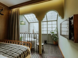 A bedroom with a large bed, a window with a view, a hanging light fixture, and a potted plant.