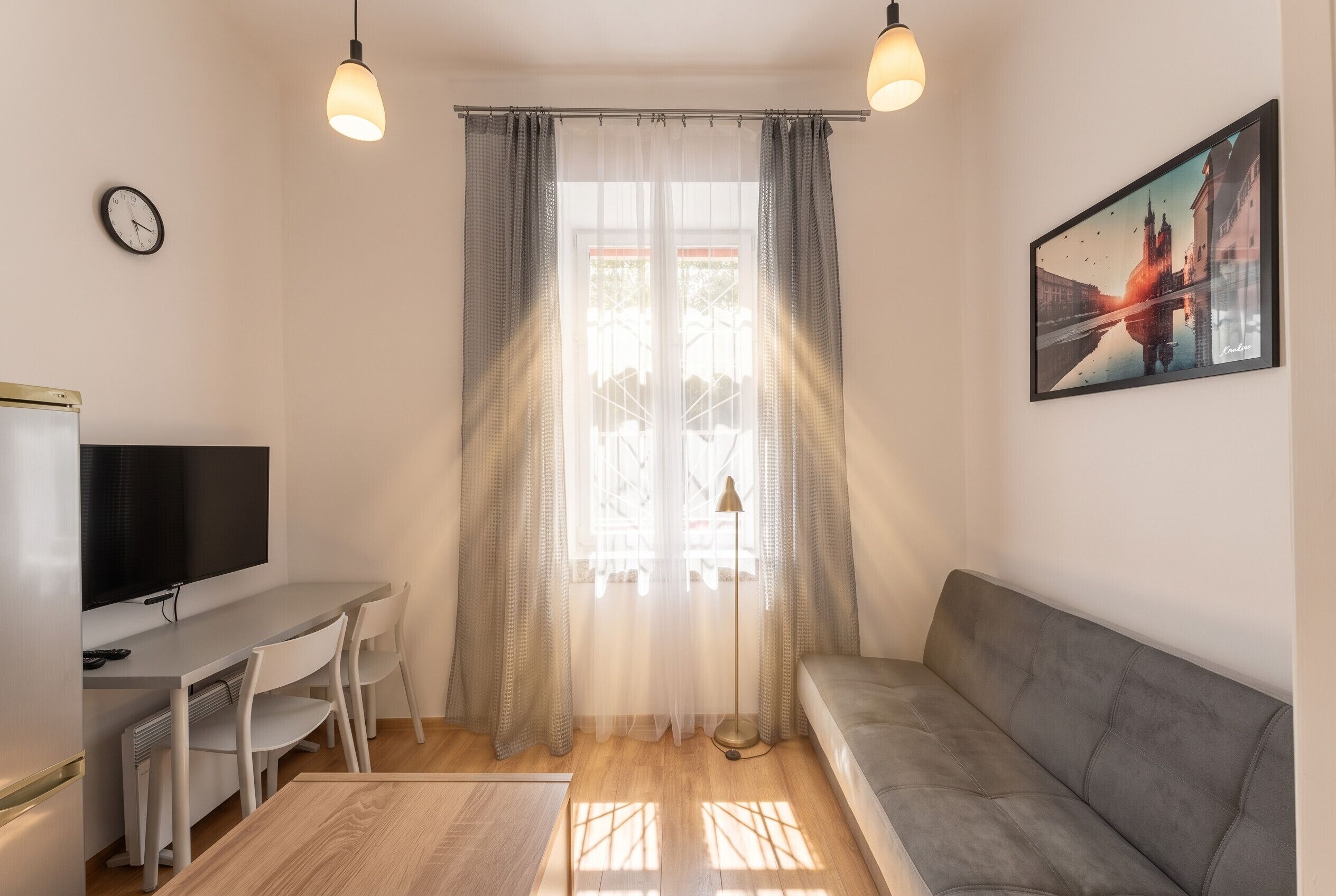 A modern living room with a sofa, a TV, a dining table with chairs, and a window with sheer curtains.
