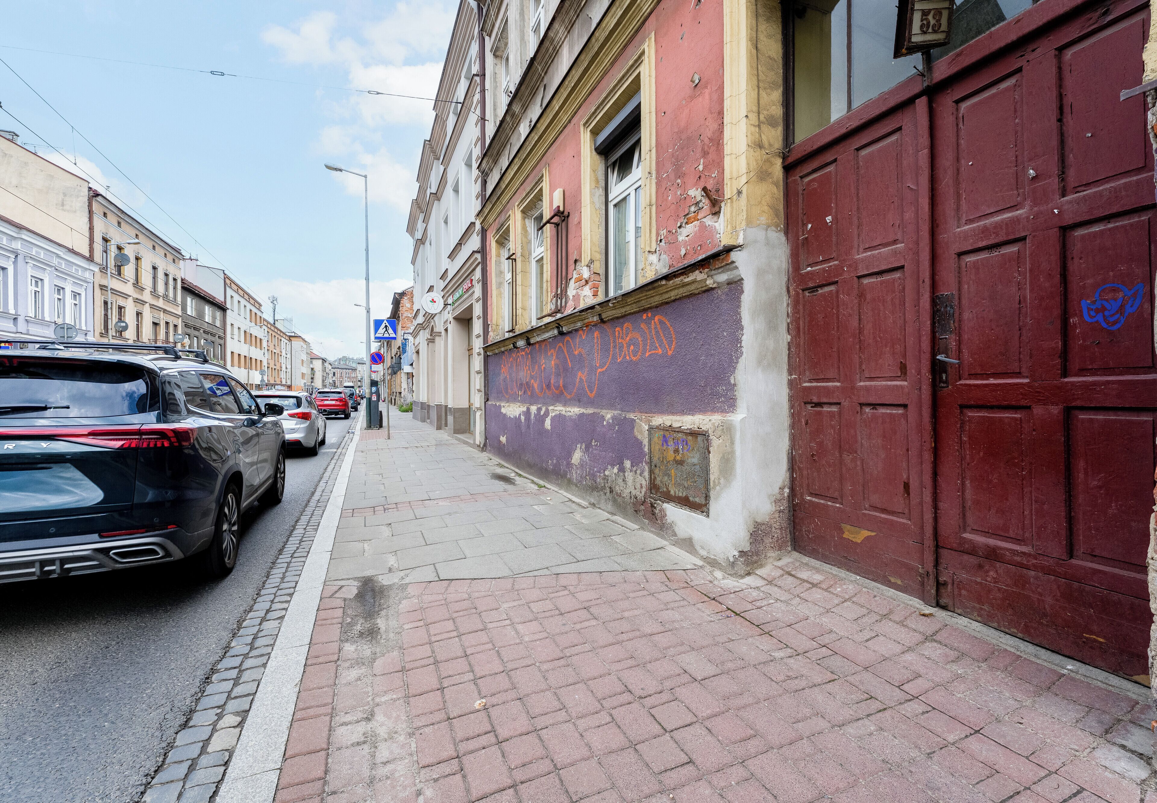 Une rue bordée de voitures garées, un trottoir et des immeubles dont on peut voir les signes d’usure.