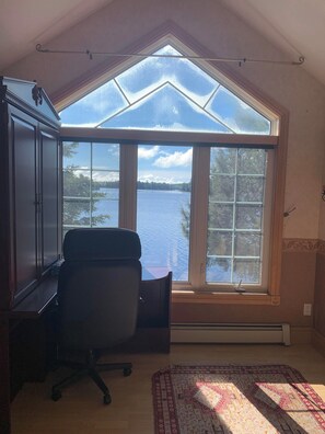 Une pièce dotée d’une grande verrière, d’un bureau, d’une chaise et offrant une vue sur un lac.