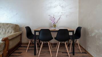 A dining area with a wooden table, four black chairs, a vase with flowers, and a sofa.