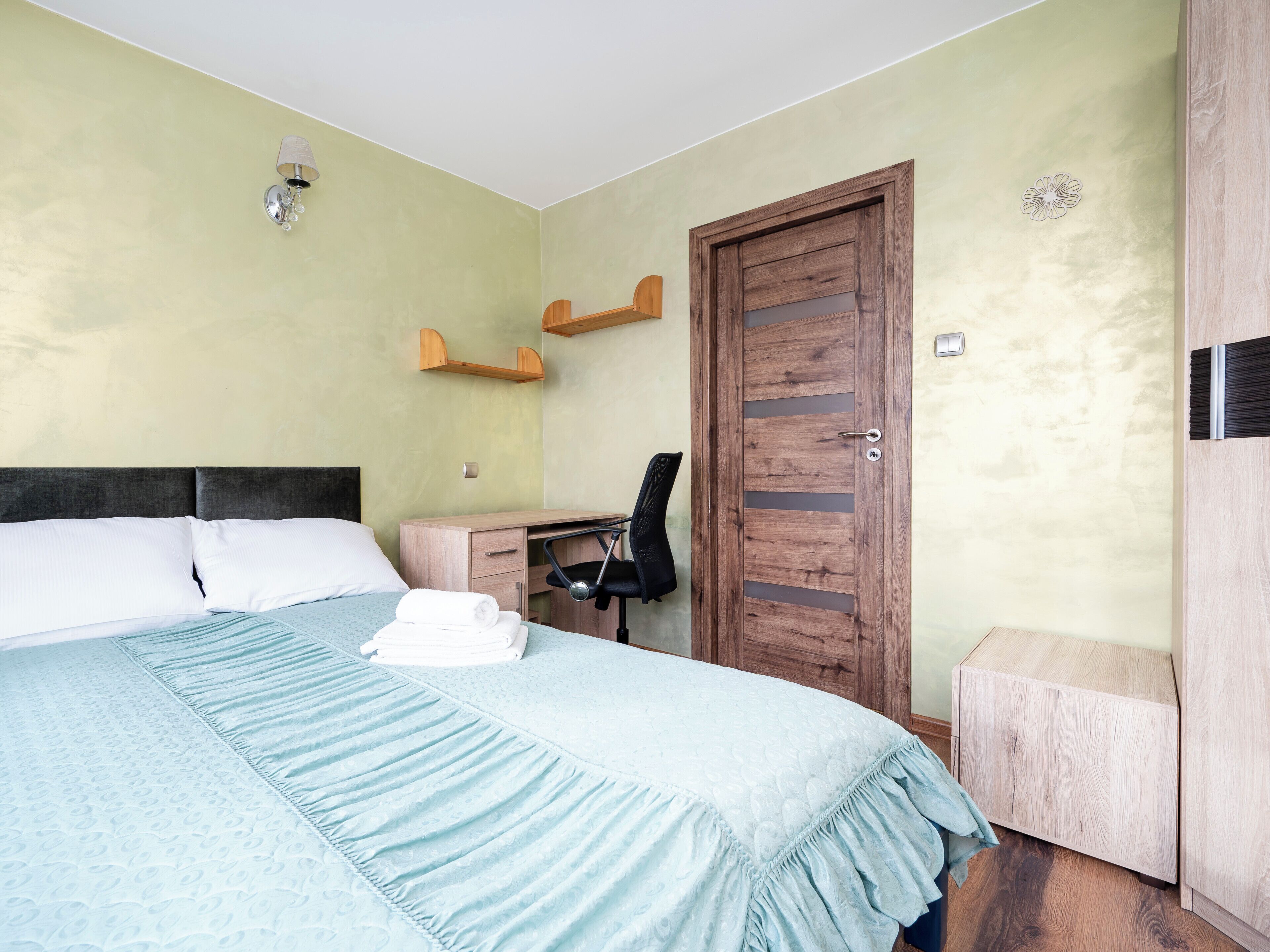 A bedroom with a bed, a desk, a chair, a wardrobe, and a door.