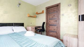 A bedroom with a bed, a desk, a chair, a wardrobe, and a door.