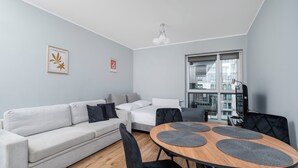 A modern living room with a sofa, a dining table with chairs, and a large window. - Park Źródliska Harmony Studio (Łódź)