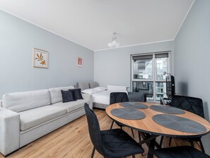 Ein stilvolles Wohnzimmer mit einer Couch, einem Esstisch mit Stühlen und einem großen Fenster.