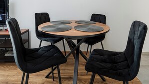 A round wooden table with four black chairs, two placemats, and a clock on the wall. - Park Źródliska Harmony Studio (Łódź)