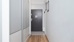 A hallway with a wooden floor, a dark door at the end, and a white wall with two framed pictures. - Park Źródliska Harmony Studio (Łódź)