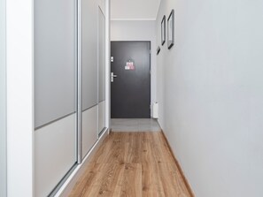 Ein Flur mit Holzboden, einer dunklen Tür am Ende und einer weißen Wand mit zwei gerahmten Bildern.